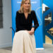 The Duchess of Edinburgh, in a black jacket and white skirt, sits in front of a Plan International banner