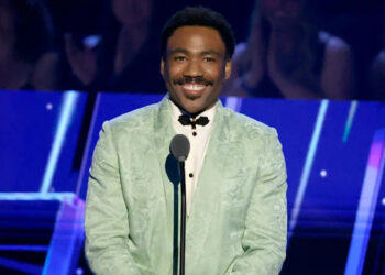 Donald Glover in a mint green suit, smiling at a microphone on stage.