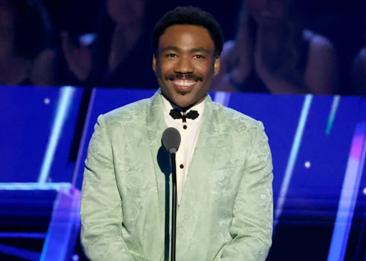 Donald Glover in a mint green suit, smiling at a microphone on stage.