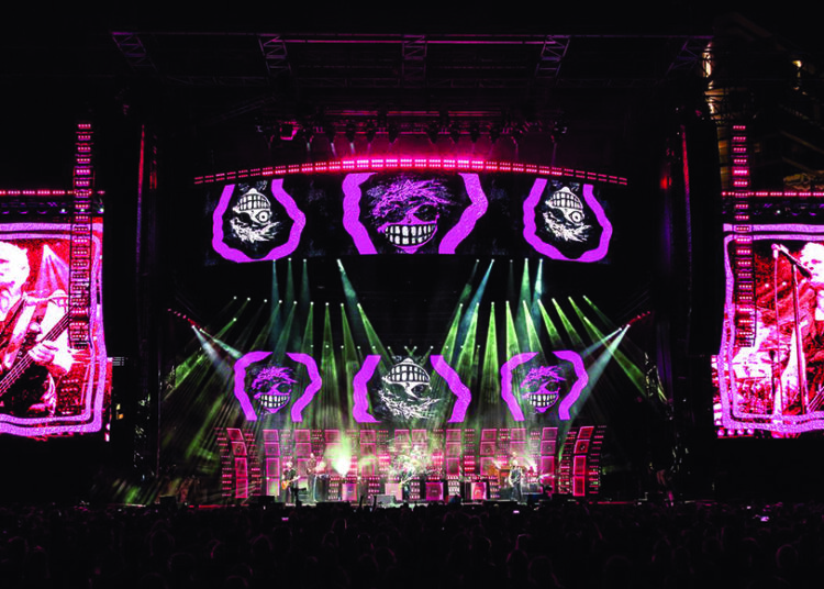 Green Day performing on large concert stage with bright LED screens and visuals