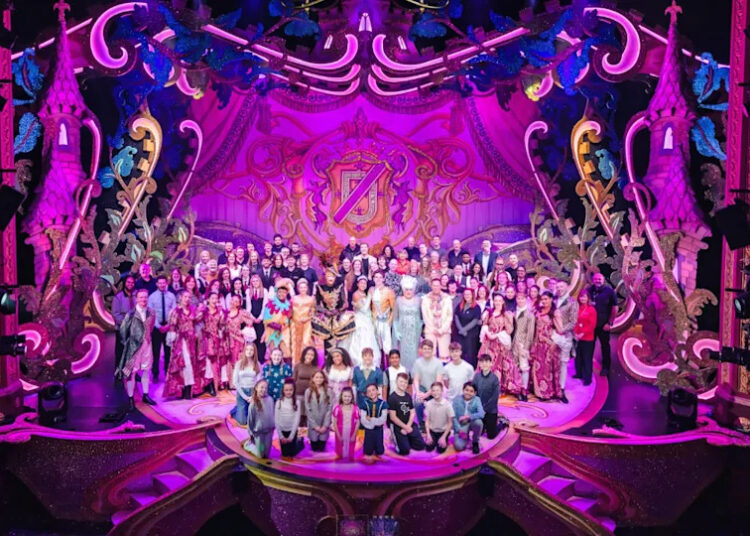 The full cast of Sleeping Beauty on the stage at Wolverhampton Grand Theatre, which is all lit up in pink.