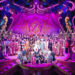 The full cast of Sleeping Beauty on the stage at Wolverhampton Grand Theatre, which is all lit up in pink.