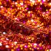An extreme close-up photograph of shimmering, glittering sequins in a variety of vibrant colors, capturing the luxurious, high-fashion aesthetic of the music industry.