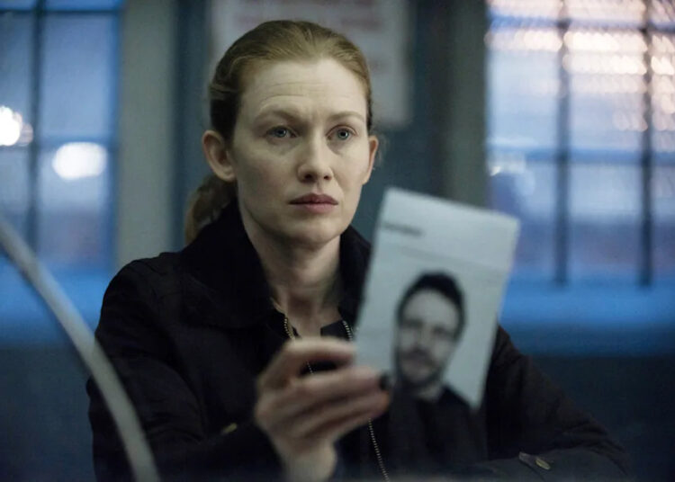 Mirielle Enos holds up a photo of a man in a scene from