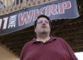 D.P. McIntire stands beneath a WKRP banner in the backyard of his home in Raleigh, N.C., on Thursday, April 2, 2026. (AP Photo/Allen G. Breed)