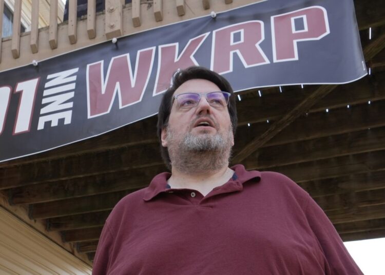 D.P. McIntire stands beneath a WKRP banner in the backyard of his home in Raleigh, N.C., on Thursday, April 2, 2026. (AP Photo/Allen G. Breed)