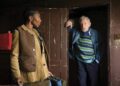 A man stands in a doorway as a woman looks back at him.