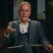 Jordan Peterson talking and gesturing with his right hand while wearing a dark suit.