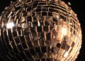 An extreme close-up photograph of shattered glass fragments reflecting bright studio lights, creating a conceptual, high-fashion aesthetic to represent the glamour and spectacle of the entertainment industry.