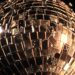 An extreme close-up photograph of shattered glass fragments reflecting bright studio lights, creating a conceptual, high-fashion aesthetic to represent the glamour and spectacle of the entertainment industry.