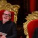 two individuals seated on ornate golden thrones one holding a card labeled taskmaster