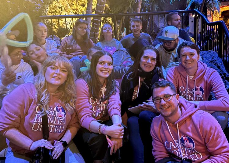 A group of people smile at the camera, many wearing sweatshirts that read "Casa Bonita United."