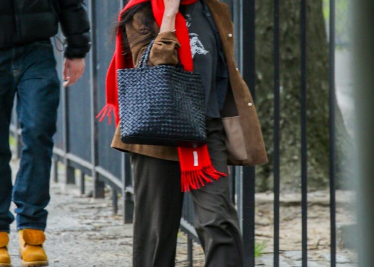 Person walking on a city sidewalk, talking on the phone, wearing a red scarf.