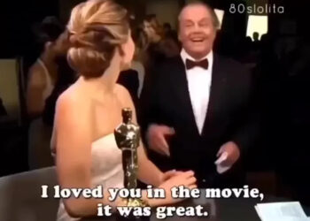 A woman in a white dress holding an Oscar statue talks to a smiling man in a tuxedo. The caption reads, "I loved you in the movie, it was great." A crowd and lights are visible in the background.
