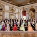 Group of elegantly dressed individuals in a formal setting with ornate architecture.