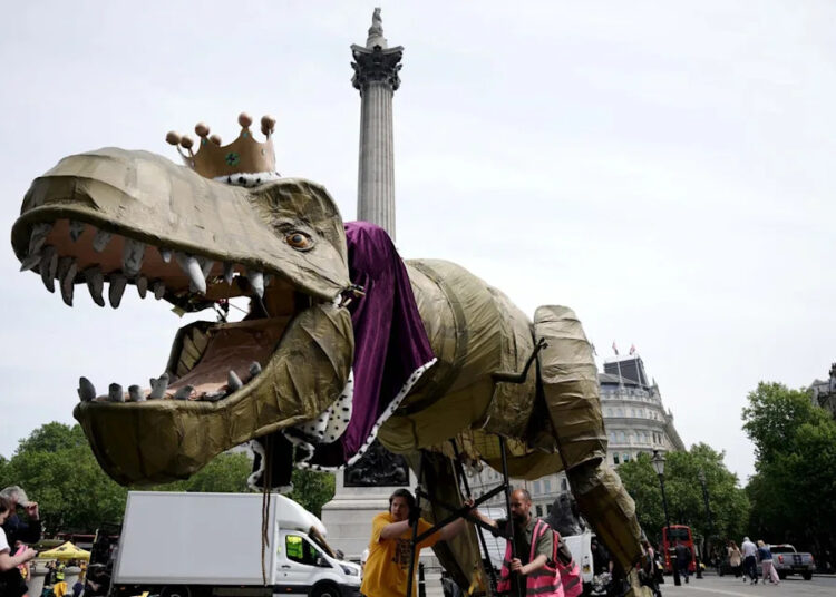 People take part in a march organised by the anti-monarchy pressure group Republic, accompanied by a fifteen-foot dinosaur mascot named Chuck the Rex, from Trafalgar Square to Buckingham Palace (PA)