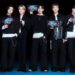 Members of BTS holding Oreo BTS packages, dressed in black and white outfits, smiling against a dark background.
