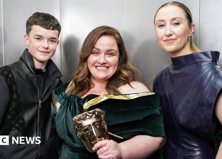Owen Cooper and Erin Doherty standing either side of a grinning Jessica Gunning, who's holding her Bafta mask trophy