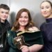Owen Cooper and Erin Doherty standing either side of a grinning Jessica Gunning, who's holding her Bafta mask trophy