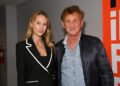 Dylan Penn and Sean Penn stand with an arm around one another. Dylan  wears a black suit with while piping while Sean  wears a black jacket over a denim shirt.