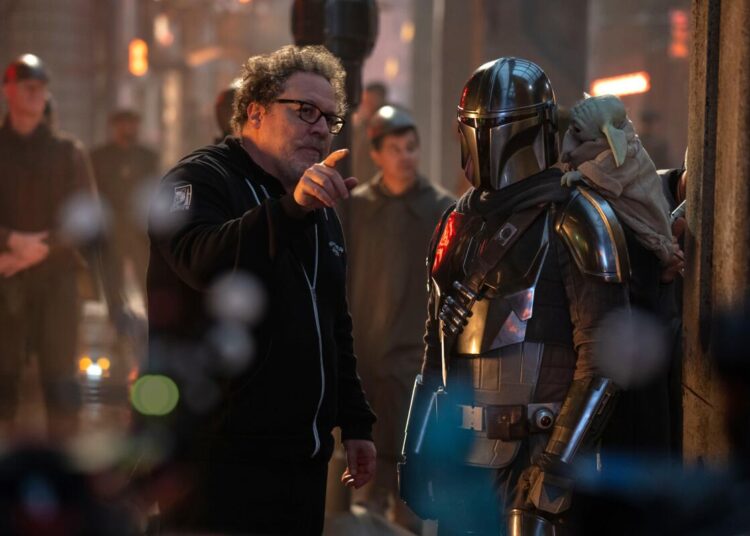 A man points a finger as he faces a helmeted person.