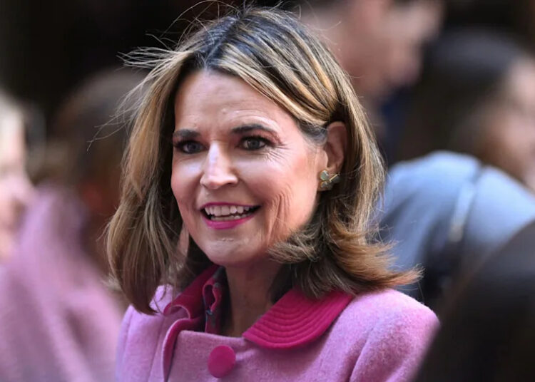 A woman with shoulder-length hair wearing a pink coat is smiling in a crowd.