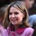 A woman with shoulder-length hair wearing a pink coat is smiling in a crowd.