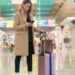 Woman looking at her smartphone to find her flight information while navigating an airport terminal with her luggage in tow.
