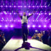 Drake energetically walks down a stage runway with purple lights and a cheering crowd.