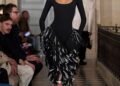 Model walking on runway in a black gown with layered ruffles