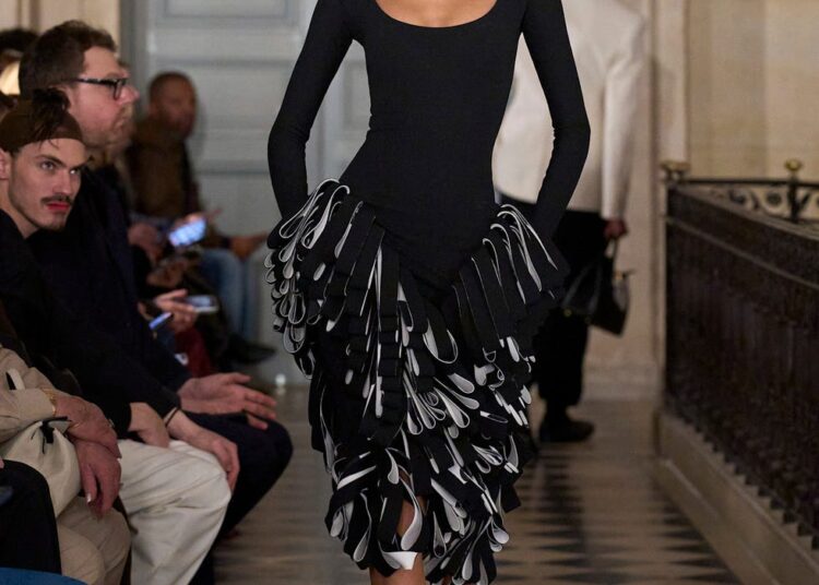 Model walking on runway in a black gown with layered ruffles