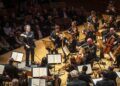 Gustavo Dudamel stands on stage with the L.A. Philharmonic orchestra.