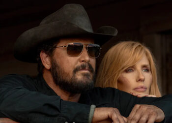 Cole Hauser in a black cowboy hat and sunglasses leans beside Kelly Reilly with a visible cheek scar, both looking ahead with serious expressions.