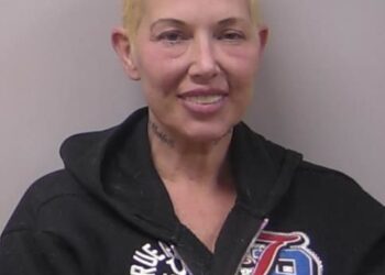 Mugshot of Kim Mathers, Eminem's ex-wife, smiling while wearing a black hoodie.