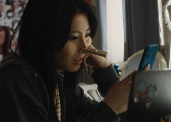 Joan, played by actor Shirley Chen, sits in her room looking at her phone with a clothes pin on her nose in Slanted.