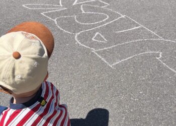 Child sitting on pavement with chalk drawing.