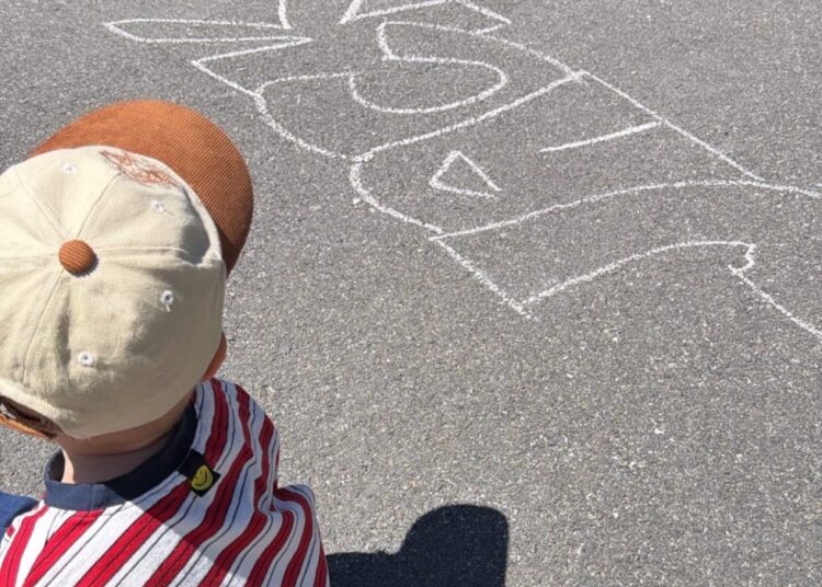 Child sitting on pavement with chalk drawing.