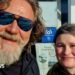 A man with a grey beard and shaggy brown hair. He's wearing mirrored sunglasses and is posing for a selfie with a young girl. She has dark hair and is wearing a black hoodie. They are both smiling.