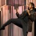 Josh Johnson doing a karate kick on stage with a chandelier installation behind him in 'Josh Johnson: Symphony'