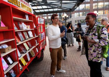 A man talks to people looking at mobile shelves filled with books.