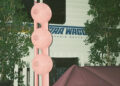 A pink sculpture with circular elements stands in front of a "Star Waggons" studio trailer, surrounded by greenery.