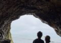 Couple standing inside a cave with ocean view.