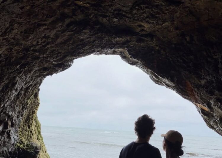 Couple standing inside a cave with ocean view.