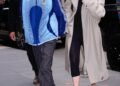 Two individuals walking on the street, one wearing a blue jacket and the other in a long beige coat.