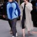 Two individuals walking on the street, one wearing a blue jacket and the other in a long beige coat.