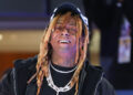 Lil Wayne smiling, wearing a black cap, dreadlocks, two diamond chains, and a grill.