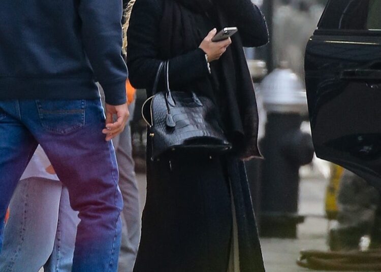 A person using a phone while standing near a car in an urban setting.