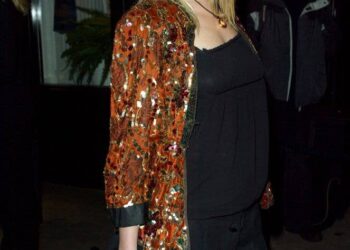 Siobhan Hewlett smiling, wearing a black dress and sequined jacket, holding a black clutch.