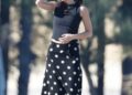 Person standing on a beach wearing a black top and a polka dot skirt.