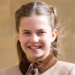 Princess Charlotte wears a light brown coat with a dark collar and smiles
